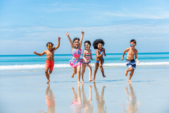 Groupe d'enfants joyeux courant sur la plage en maillots de bain colorés et lunettes de soleil — vêtements de plage pour enfants.