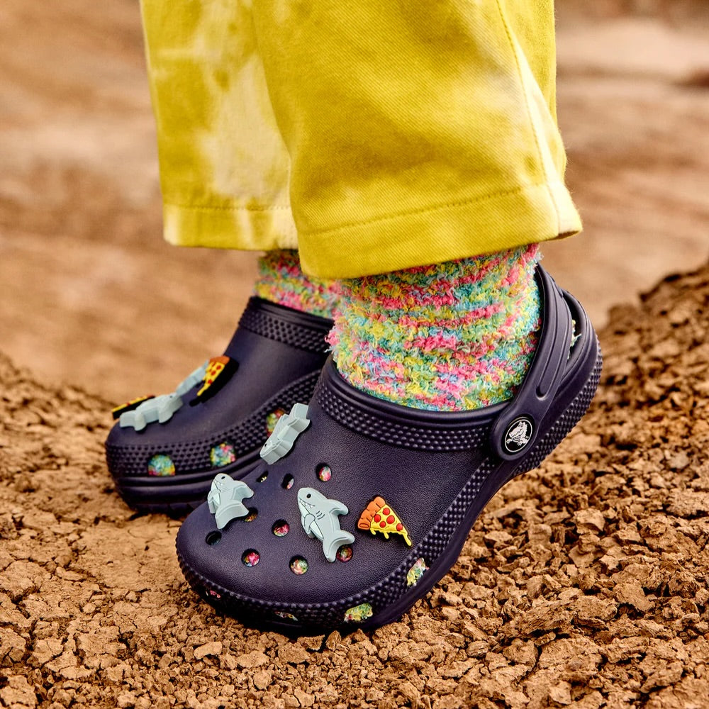 Enfant portant des Crocs Classic marine décorés de Jibbitz requins et pizza avec des chaussettes multicolores — sabots Crocs pour enfants.