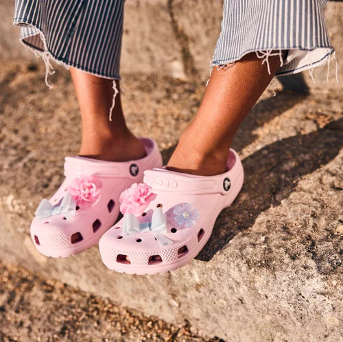 Enfant portant des Crocs Classic rose pâle décorés de Jibbitz fleurs et papillon — sabots Crocs roses pour fille.