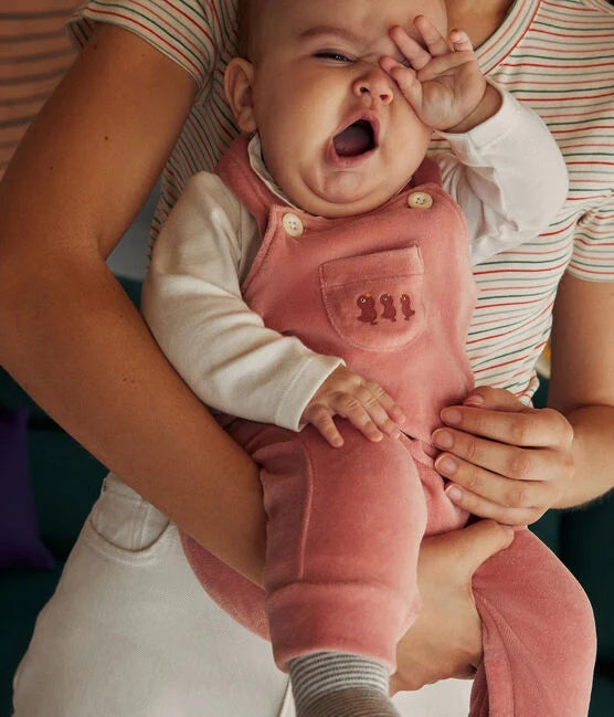 Un bébé endormi portant une salopette rose et un cache-couche à manches longues blanc.