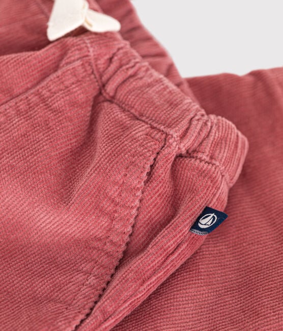 Un pantalon pour bébé en velours rose côtelé avec poches latérales et étiquette Petit Bateau.