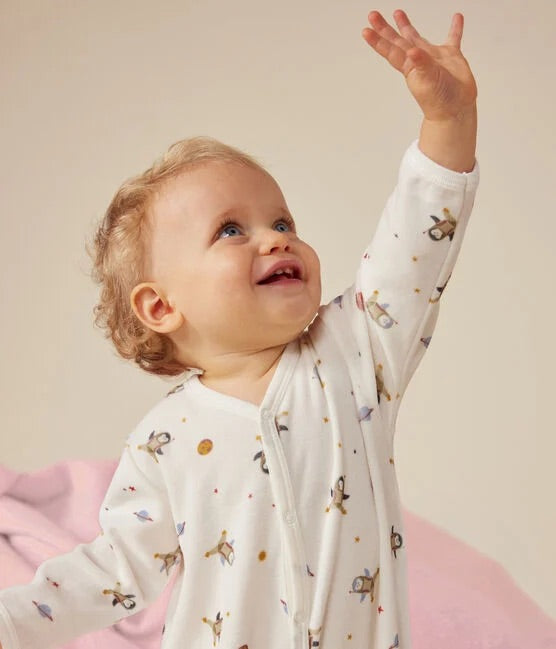 Un bébé portant un pyjama blanc à motif d'illustration de pingouins dans l'espace, avec des étoiles.
