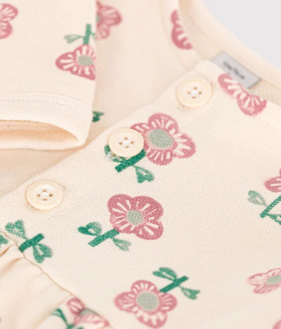 Une robe pour bébé à col rond et bouton à l'avant. Couleur crème et fleuri rose.