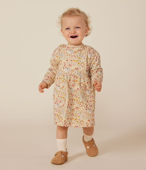 Une robe pour bébé à col rond, couleur crème et motif de petites fleurs colorées.