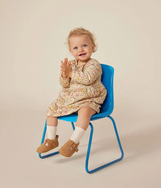 Une robe pour bébé à col rond, couleur crème et motif de petites fleurs colorées.