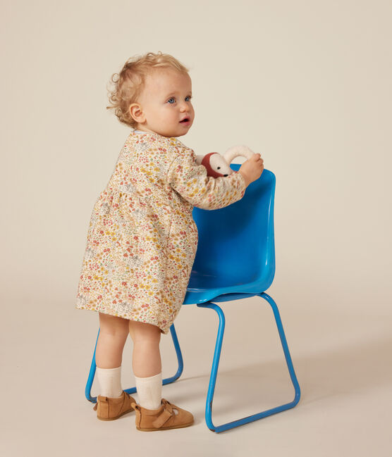 Une robe pour bébé à col rond, couleur crème et motif de petites fleurs colorées.