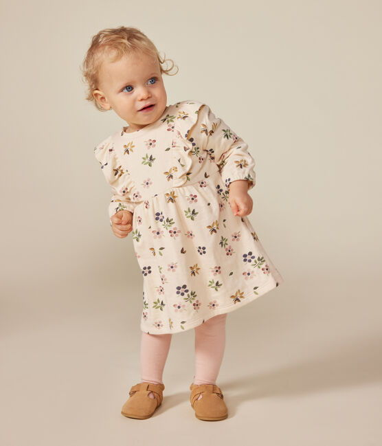 Une robe pour bébé beige et fleurie rosé, vert et bleu, avec des volants sur la poitrine.