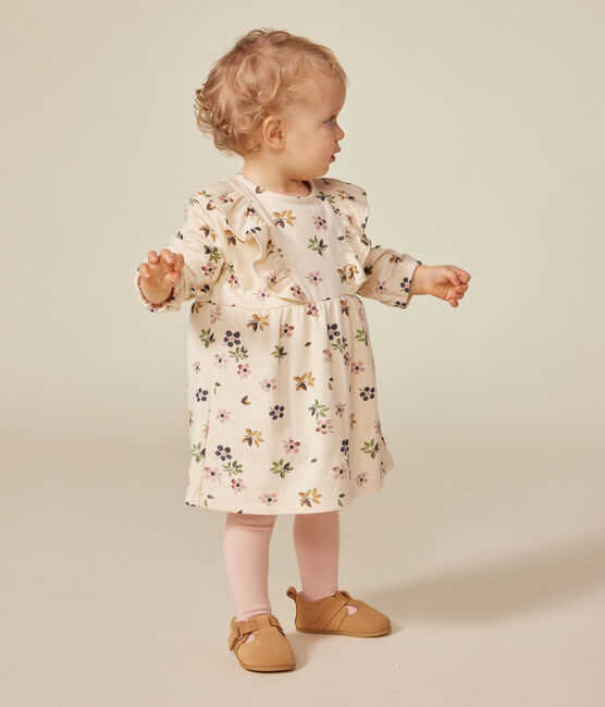 Une robe pour bébé beige et fleurie rosé, vert et bleu, avec des volants sur la poitrine.