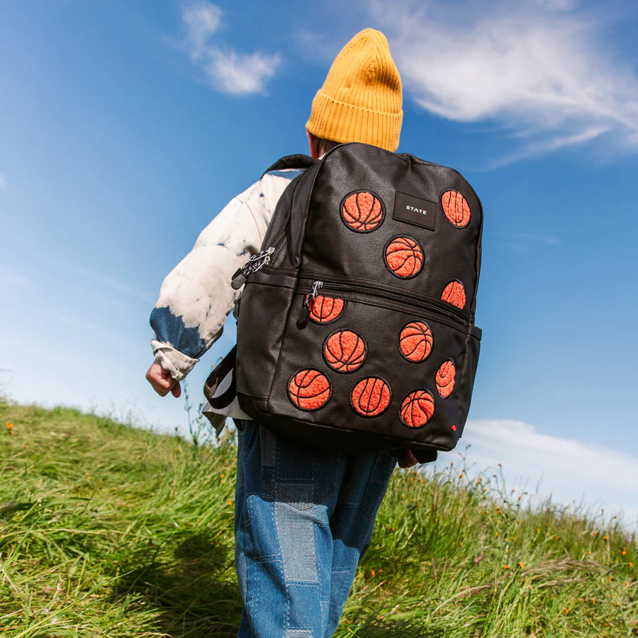 Un enfant dans un champs avec un sac à dos noir à motif de basketballs.