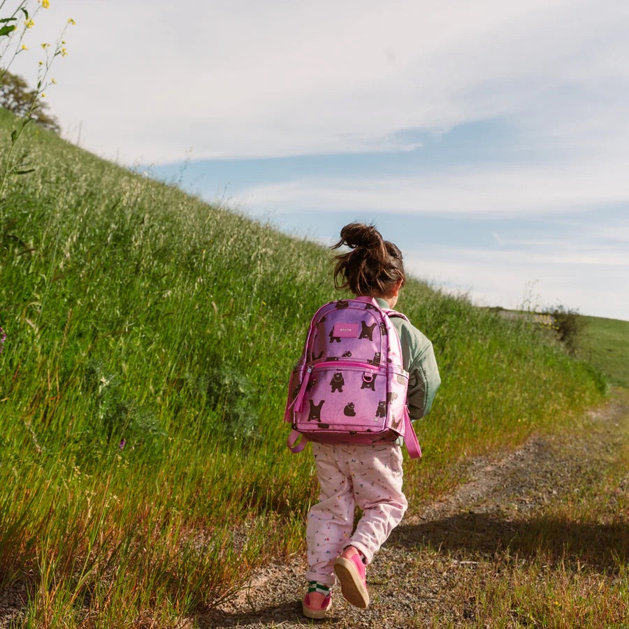 Une fillette courant dans un champs et portant le sac à dos rose.