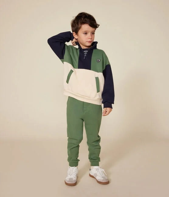 Un garçon portant un sweatshirt colorblock en noir, vert et beige, avec zipper au col et poches.