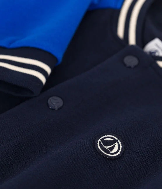 Une veste style Teddy aux manches bleu éclatant et corps foncé, col rayé blanc et poignet élastique.