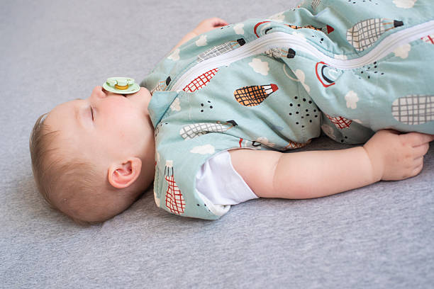 Bébé endormi portant une gigoteuse à imprimés colorés avec fermeture éclair — vêtement de nuit sécuritaire pour nourrisson.