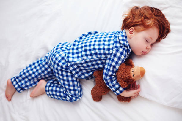 Enfant endormi en pyjama à carreaux bleu et blanc serrant un ourson en peluche — pyjama confortable pour bébé et tout-petit.
