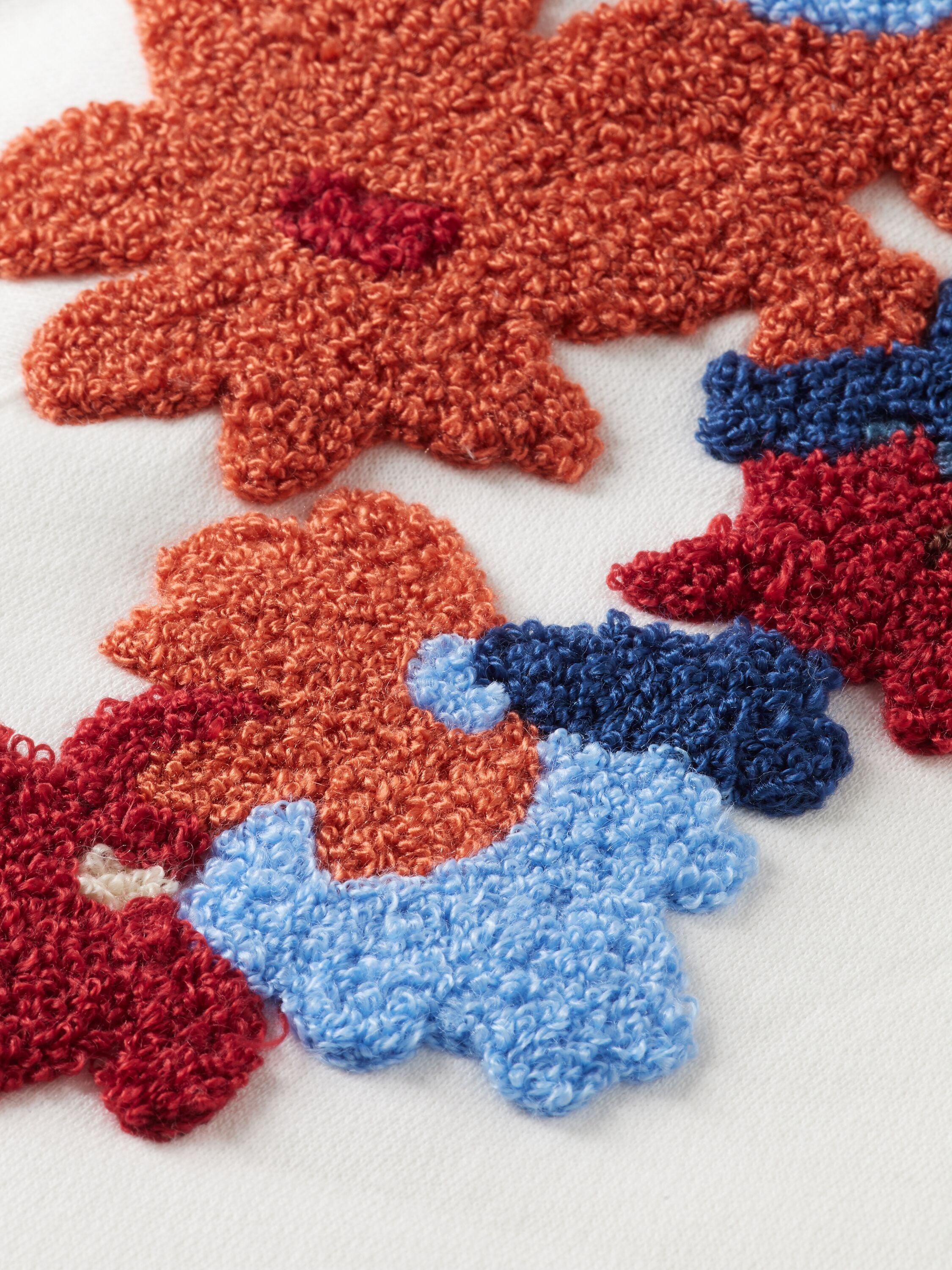 Détail d'une broderie de fleur orange et bleu.