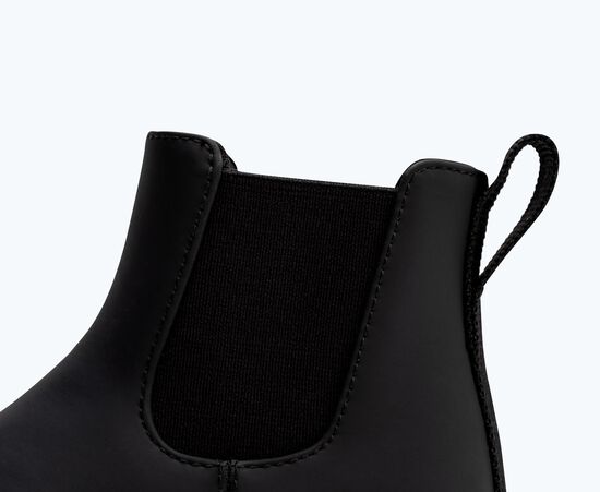 Une botte Chelsea noire avec semelle et panneaux élastiques noirs.