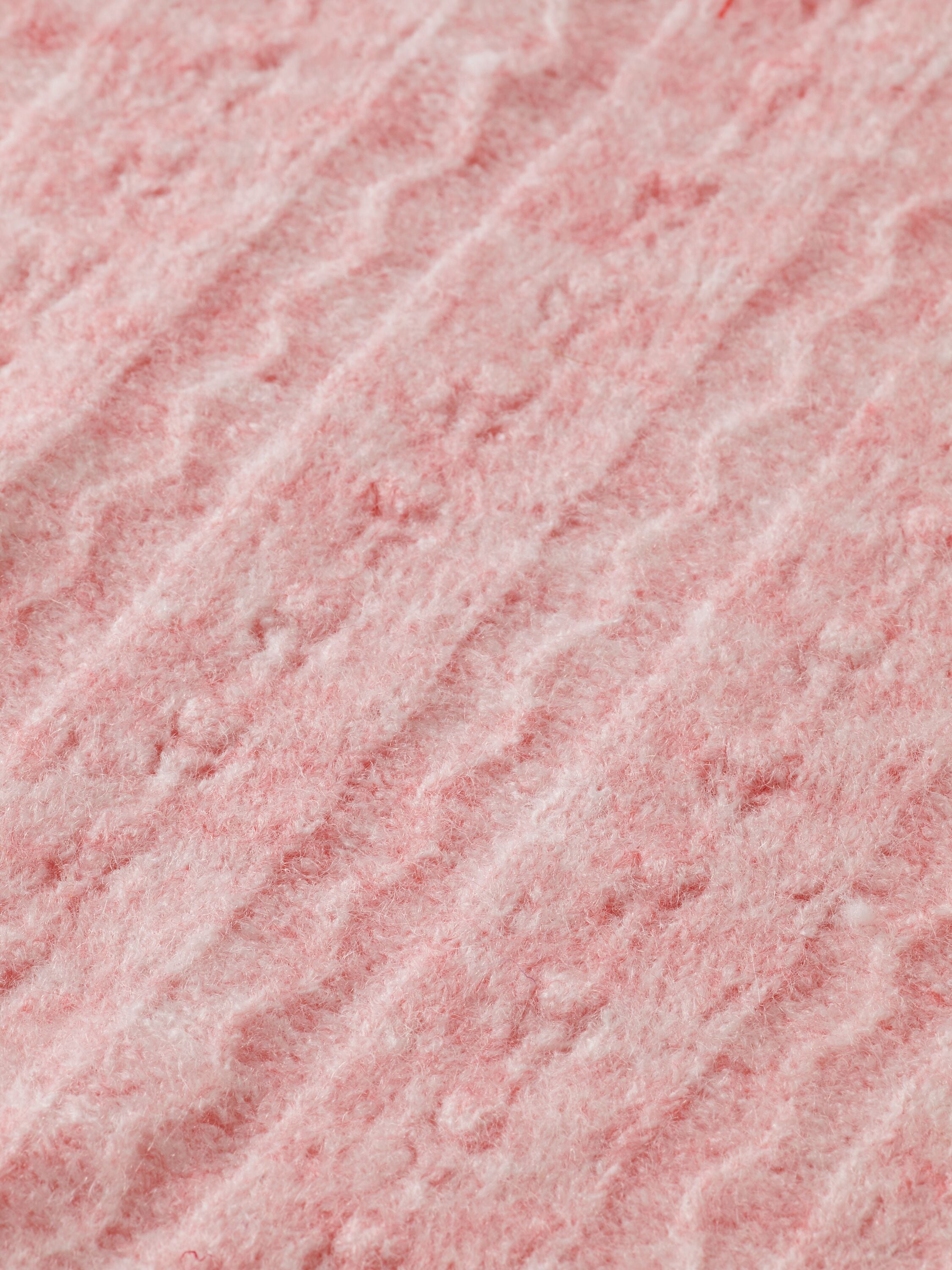 Zoom sur la texture côtelée d'un tricot de couleur rose pêche.