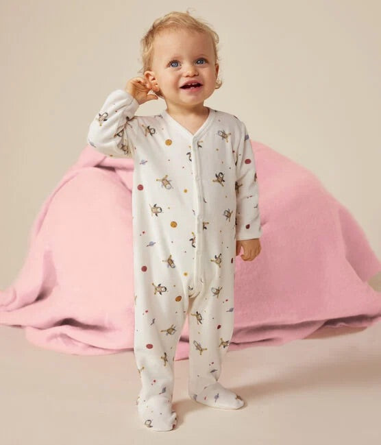 Un bébé portant un pyjama blanc à motif d'illustration de pingouins dans l'espace, avec des étoiles.