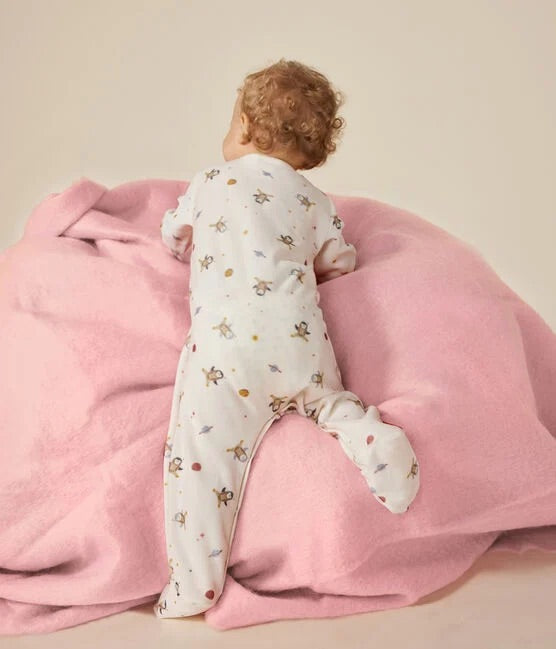 Un bébé portant un pyjama blanc à motif d'illustration de pingouins dans l'espace, avec des étoiles.