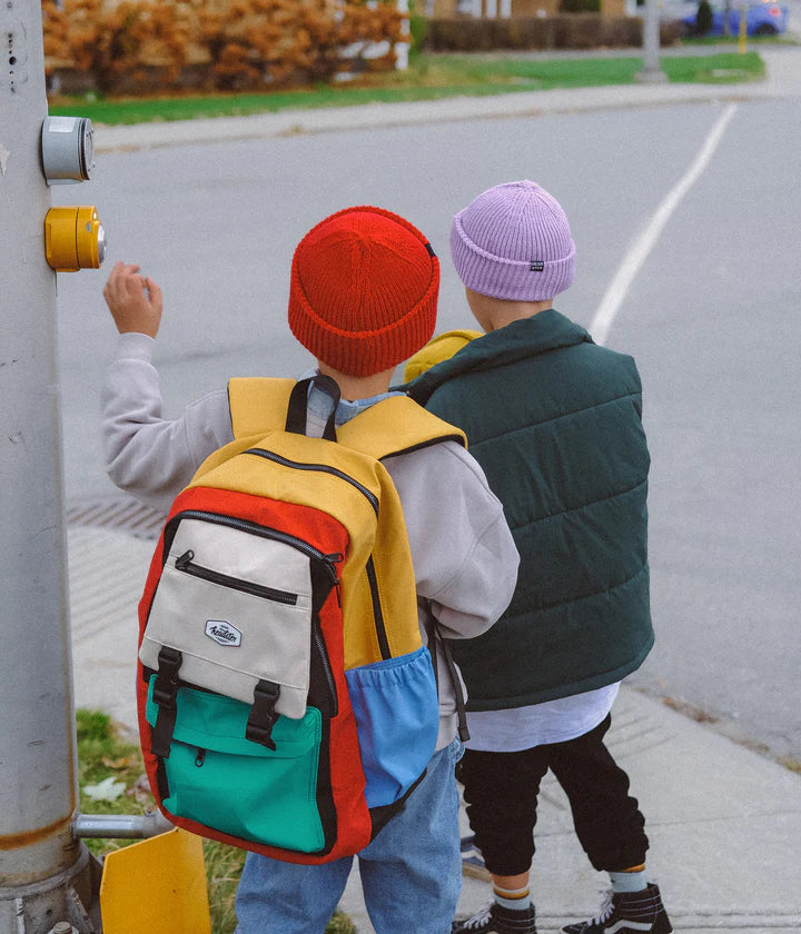 Un enfant portant un sac à dos vert, beige, bleu et jaune.