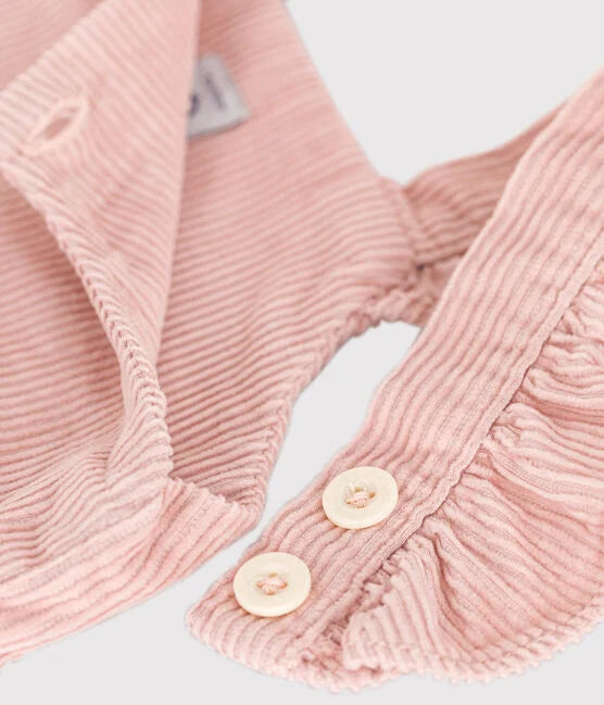 Salopette pour bébé en velours rose avec volant sur les bretelles et ouverture à boutons.